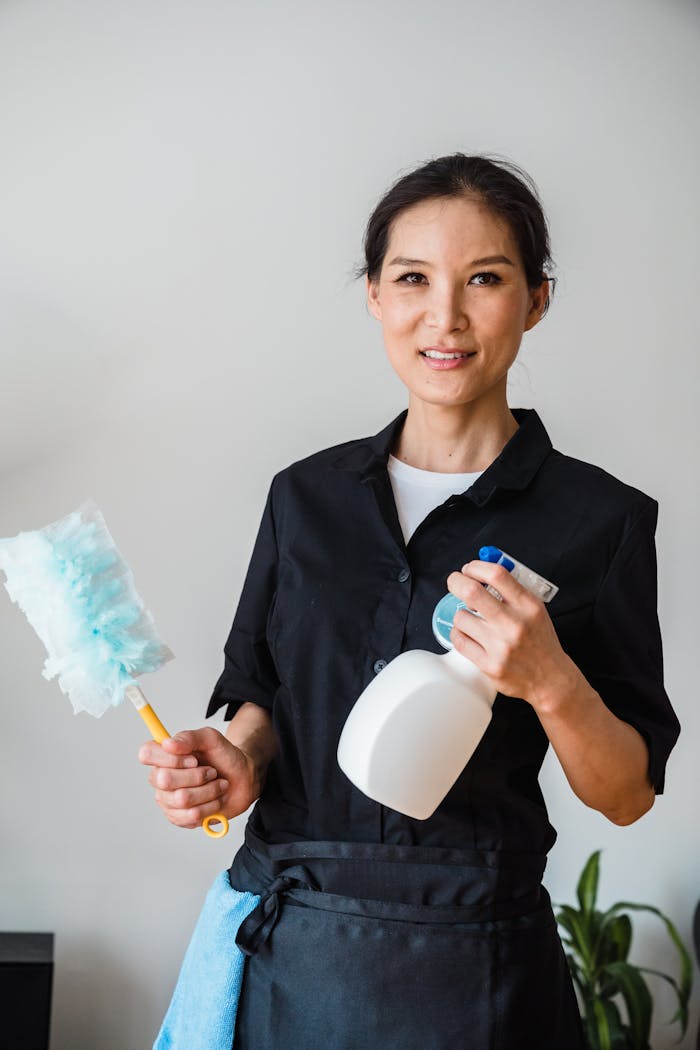 hero-img-01 A female housekeeper smiling while holding cleaning tools indoor.